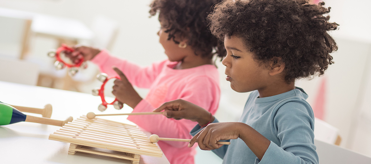 This is a stock photo from Shutterstock. There are two children sitting at a table playing with toys. The toys are various musical instruments. The little girl is wearing a pink long sleeve shirt and gold earrings. The little boy is wearing a blue long sleeve shirt.