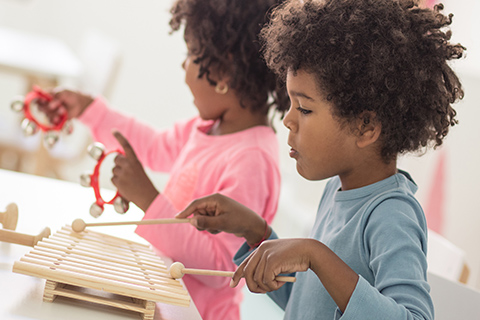 This is a stock photo from Shutterstock. There are two children sitting at a table playing with toys. The toys are various musical instruments. The little girl is wearing a pink long sleeve shirt and gold earrings. The little boy is wearing a blue long sleeve shirt.